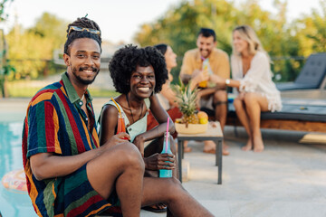 Young couple enjoying drinks by the pool at a summer party