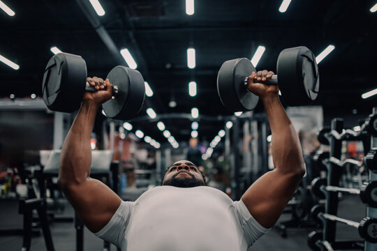 Determined bodybuilder lifting heavy dumbbells during intense workout session