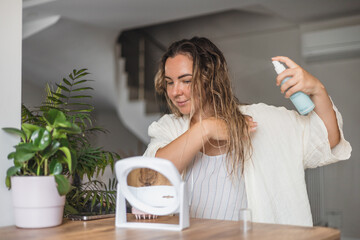 Woman styling wet hair with spray in a bright indoor space during the daytime