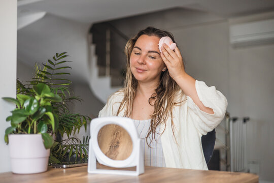 Woman ,aking sculp head massage and applying hair product while looking in a mirror in a modern indoor setting