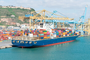 Container ship docked at busy port with cranes and hillside view