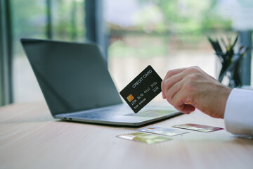 Close-up of man's hands inside the office, businessman in blue shirt and white t-shirt works at workplace, man holds bank credit card and smartphone, makes online purchase in online store.