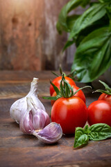Traditional Italian food ingredients. Fresh red tomatoes, garlic and fresh green basil leaves on rustic old barn wood background.