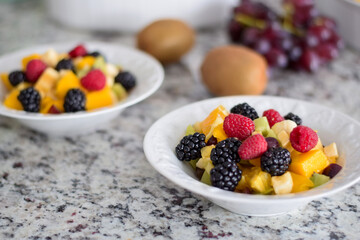Bowl with cut up fresh fruit and berries on kitchen counter
