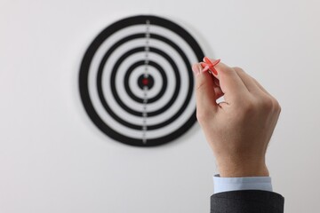 Targeting. Man with arrow aiming at dart board on light background, closeup