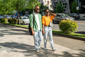 Cheerful African American girl and guy on romantic date, strolling along street chatting joking laughing loudly. Overjoyed girlfriend boyfriend spend leisure time together, enjoying joyful strolling.