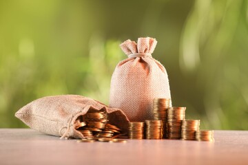 Burlap bags and stacked coins on table against blurred background