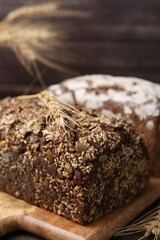 Freshly baked loaves of bread and spikes on table against brown background, closeup