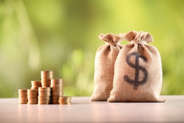 Burlap bags and stacked coins on table against blurred background