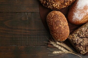 Freshly baked loaves of bread and spikes on wooden table, flat lay. Space for text