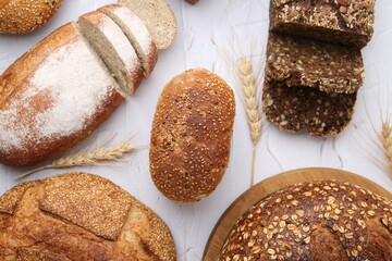 Freshly baked loaves of bread and spikes on light textured table, flat lay