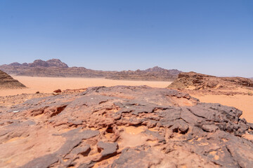 Arid Grandeur: Panorama of the desolate desert landscape, a sweeping vista of sunbaked sand dunes and distant rock formations under a clear blue sky.