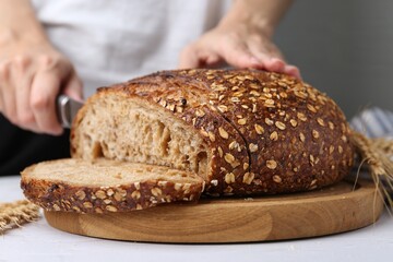Woman cutting freshly baked bread at light table against grey background, closeup