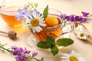 Aromatic herbal tea in glass cups, different flowers and mint on beige background, closeup