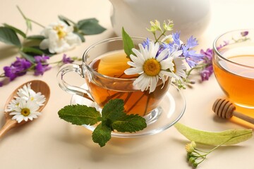 Aromatic herbal tea in glass cups, different flowers, mint and teapot on beige background, closeup