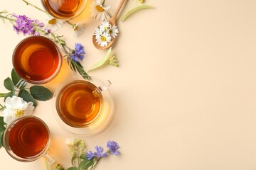 Aromatic herbal tea in glass cups and different flowers on beige background, flat lay. Space for...