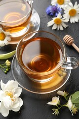 Aromatic herbal tea in glass cups and different flowers on black table, above view