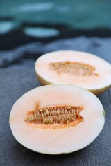 Halves of juicy melon on grey surface near swimming pool, closeup