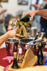 Wine tasting event with hand pouring white wine into glass, surrounded by wine bottles, ice buckets and wooden trays. Concept of celebration, sommelier service and premium lifestyle