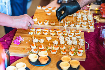 Hands placing gourmet appetizers with toothpicks on wooden trays at catering event. Concept of fine dining, finger food, festive culinary, catering, party food