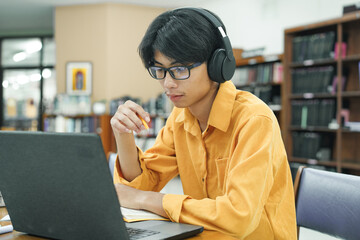 Young collage student using computer and mobile device studying online in library.