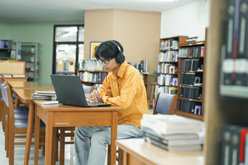 Attractive young male university student using a laptop while studying in library.