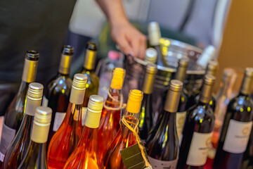 Closeup of assorted wine bottles with man sommelier in background arranging drinks on event table. Concept of wine tasting, celebration and sommelier service at festival