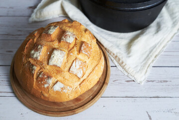 Freshly baked sourdough bread resting on wooden board near cast iron pot