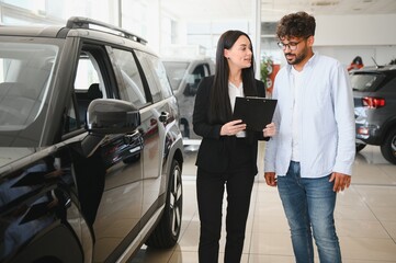 Saleswoman showing new car to customer in dealership