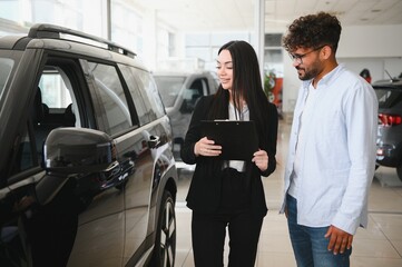 Saleswoman showing new car to customer in dealership