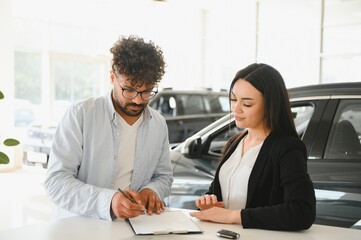 Fototapeta premium Customer signing contract for new car in dealership with saleswoman