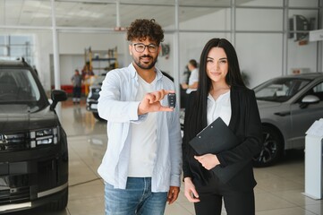 Happy customer showing new car key with saleswoman at dealership