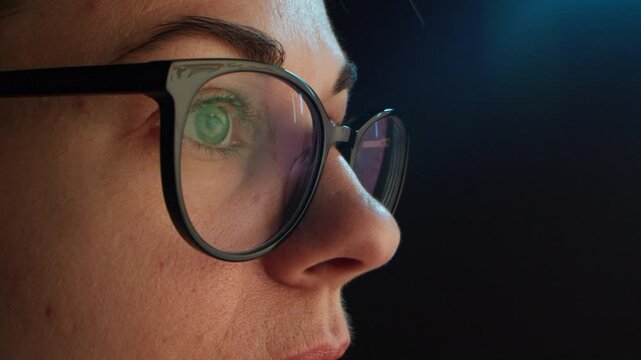 Close up of tired woman working at night on laptop, girl in eye glasses with reflections overworking busy, using computer in dark office