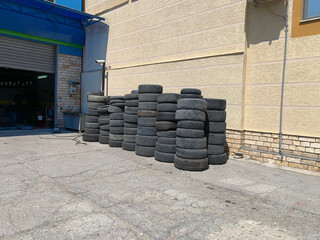 Stack of used car tires near the wall of a building on asphalt in a sunny day. Urban scene next to an auto repair shop.