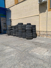 Stack of used car tires near the wall of a building on asphalt in a sunny day. Urban scene next to an auto repair shop.
