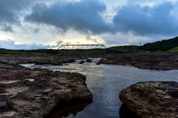 River flowing through rocky landscape with a bridge in the distance in Meghalaya. 