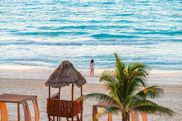 Peaceful beach scene with a woman standing by the shore in Cancun, surrounded by turquoise waves and tropical palm trees High-quality photo