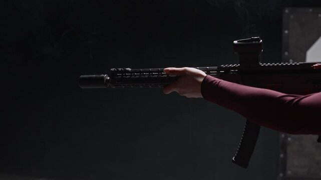 Side view of Caucasian woman in goggles shooting then reloading rifle during training at indoor range, copy space