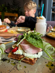 Cheese waffles with ham, cream cheese and cucumber with cutlery. Delisious savory breakfast.