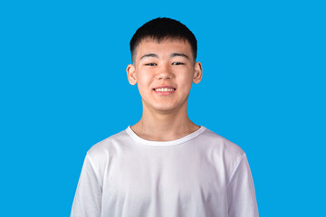 Portrait of handsome smiling asian boy in white T-shirt against blue background
