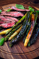 Grilled green, white and violet asparagus with roasted dry aged beef steak served as close-up on rustic wooden board