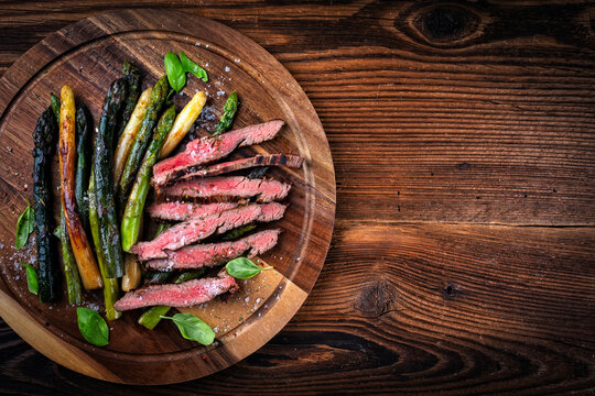 Grilled green, white and violet asparagus with roasted dry aged beef steak served as top view on rustic wooden board - Powered by Adobe