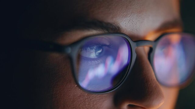Eyes glasses reflecting diagrams at dark place closeup. Concentrated trader face