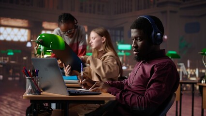 Young adult listening to study music and writing ideas for bachelor paper, using ambient sounds to help with concentration in the campus library. Girl student does academic research. Camera A.