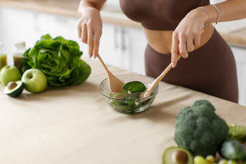 Closeup of woman in sportswear mixing healthy fresh vegetables salad in bowl, cooking healthy meal in kitchen at home