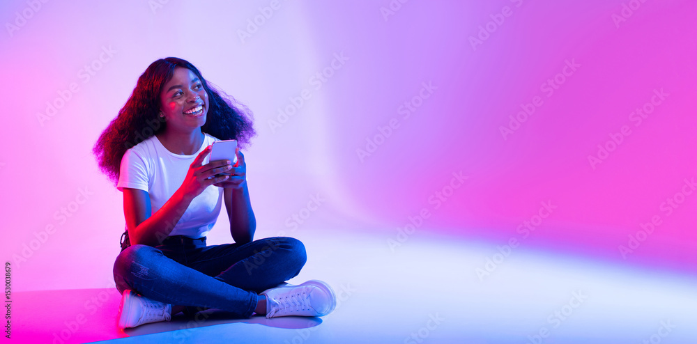 Poster amazing application. young black lady using modern smartphone and looking at copy space in neon ligh