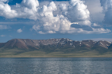 Wide angle landscape - highland lake, snow-capped mountains, blue sky with white clouds. Song Kul Lake, Naryn Region, Kyrgyzstan, Central Asia.  