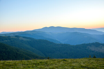 Serene mountain view during sunrise showcasing layers of hills and a grassy foreground. Captures natural beauty perfect for conveying peace, wilderness, and outdoor exploration. Carpathians, Ukraine