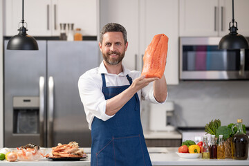 Man cook trout in apron. Cooking fish at home. Mature professional man cook trout fillet. Seafood cuisine. Cooking healthy food. Chef man hold trout fish fillet. Best quality