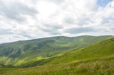 Serene view of rolling green hills and mountains under a partly cloudy sky. Captures the essence of...